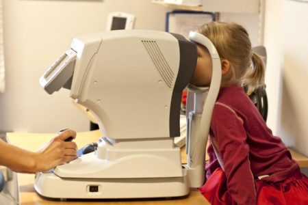 Eye doctor using eyesight testing equipment to treat a young patient